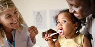 A smiling healthcare professional and a parent help a young child brush their teeth.